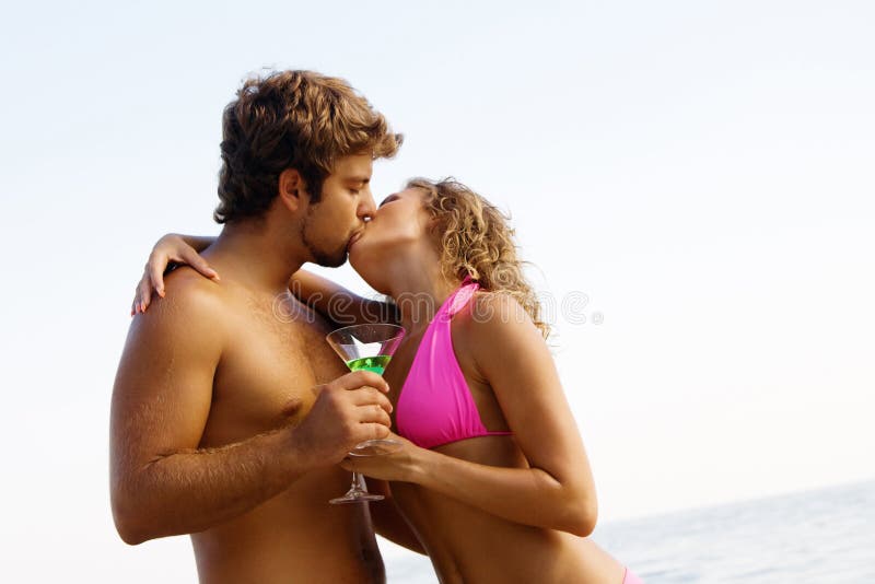 La giovane coppia con i cocktail sta baciando fotografia stock La giovane coppia con i cocktail sta baciando fotografia stock
