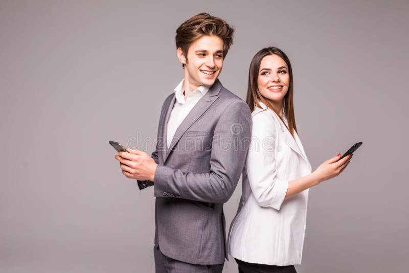 La giovane coppia sta utilizzando gli Smart Phone e sta sorridendo mentre stava di nuovo alla parte posteriore su un fondo grigio immagine stock libera da diritti La giovane coppia sta utilizzando gli Smart Phone e sta sorridendo mentre stava di nuovo alla parte posteriore su un fondo grigio immagine stock libera da diritti