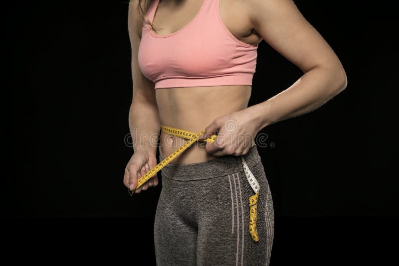 La giovane donna con un corpo atletico utilizza un nastro di misurazione fotografia stock La giovane donna con un corpo atletico utilizza un nastro di misurazione fotografia stock