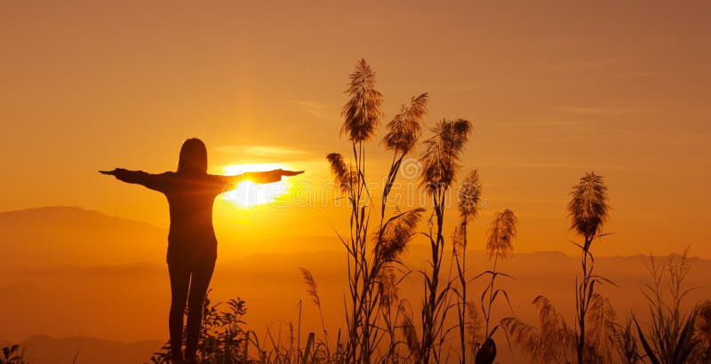 La giovane donna della siluetta del tramonto che ritiene alla libertà e si rilassa