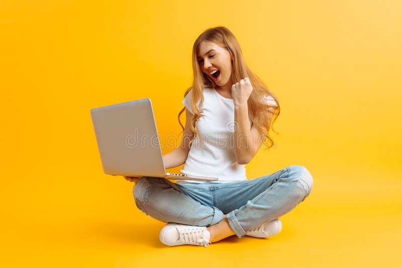 La giovane donna felice sta sedendosi facendo uso del computer portatile e sta celebrando la vittoria ed il successo sopra fondo fotografia stock La giovane donna felice sta sedendosi facendo uso del computer portatile e sta celebrando la vittoria ed il successo sopra fondo fotografia stock