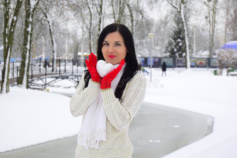 La giovane donna le tenute castane una palla di neve sotto forma di cuore fotografie stock La giovane donna le tenute castane una palla di neve sotto forma di cuore fotografie stock