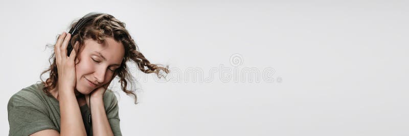 La giovane donna riccia allegra spensierata ascolta musica favorita con le sue cuffie stereo fotografia stock La giovane donna riccia allegra spensierata ascolta musica favorita con le sue cuffie stereo fotografia stock