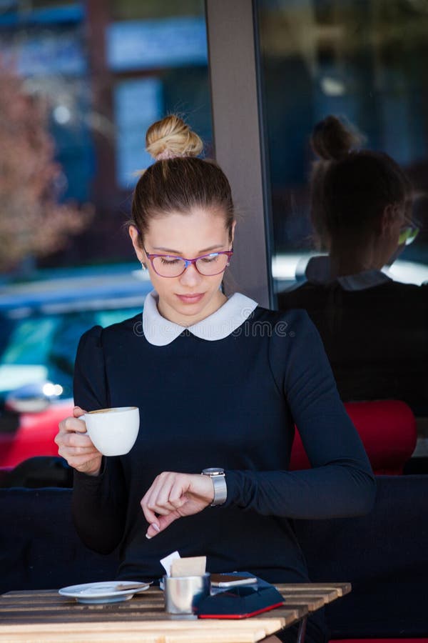 La giovane donna si siede in caffè all'aperto aspettando qualcuno che esamina w fotografia stock libera da diritti La giovane donna si siede in caffè all'aperto aspettando qualcuno che esamina w fotografia stock libera da diritti