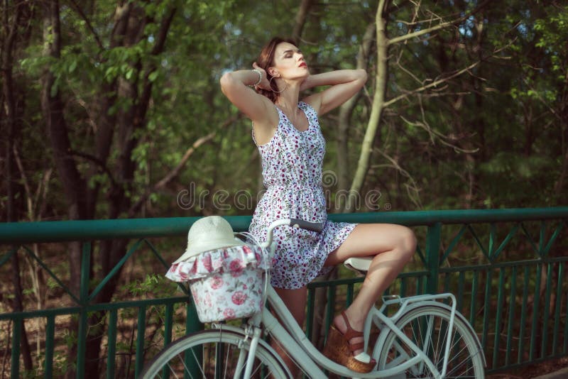 La giovane donna sta con una bicicletta sul ponte fotografia stock La giovane donna sta con una bicicletta sul ponte fotografia stock