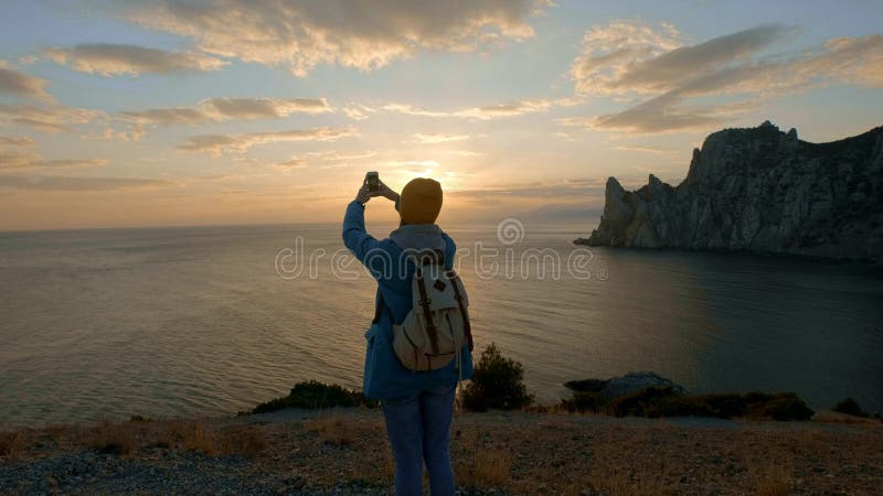 La giovane escursione attraente della ragazza fa la foto sullo smartphone Spara un bello tramonto su un capo dal mare Ha raggiunt