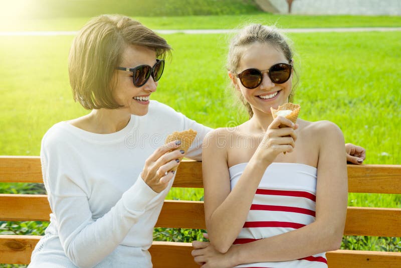 La giovane madre felice e la figlia sveglia di un adolescente in una città parcheggiano il cibo del gelato, la conversazione e la immagini stock libere da diritti La giovane madre felice e la figlia sveglia di un adolescente in una città parcheggiano il cibo del gelato, la conversazione e la immagini stock libere da diritti