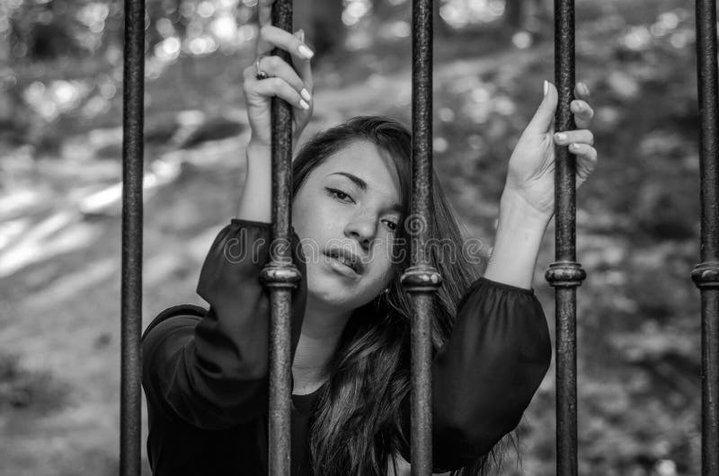 La giovane ragazza affascinante l'adolescente con capelli lunghi che si siedono dietro le barre nel prigioniero della prigione in fotografia stock La giovane ragazza affascinante l'adolescente con capelli lunghi che si siedono dietro le barre nel prigioniero della prigione in fotografia stock