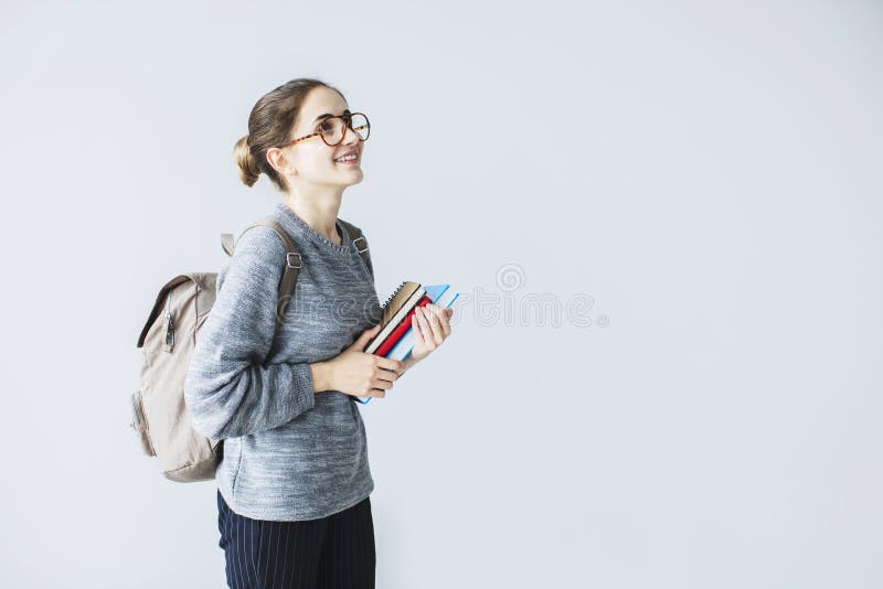 Happy young female student looking upwards carrying back pack holding books. Happy young female student looking upwards carrying back pack holding books