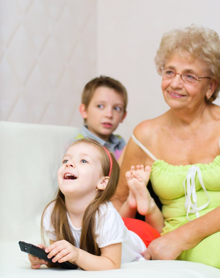 La grand-mère avec ses petits-enfants regardent la TV image stock La grand-mère avec ses petits-enfants regardent la TV image stock