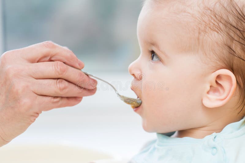 La grand-mère donne l'aliment pour bébé d'une cuillère photographie stock libre de droits La grand-mère donne l'aliment pour bébé d'une cuillère photographie stock libre de droits