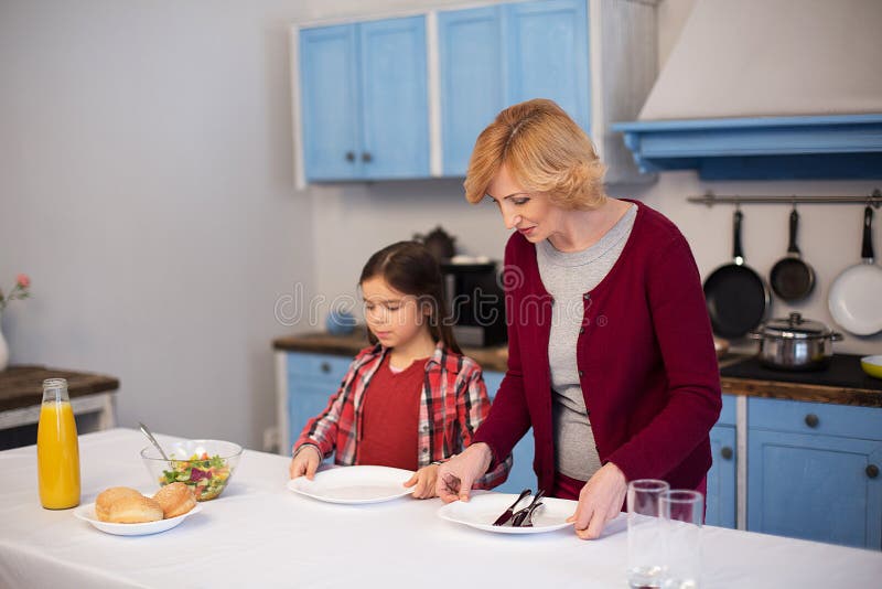 La grand-mère et la petite-fille étendent la table image libre de droits La grand-mère et la petite-fille étendent la table image libre de droits