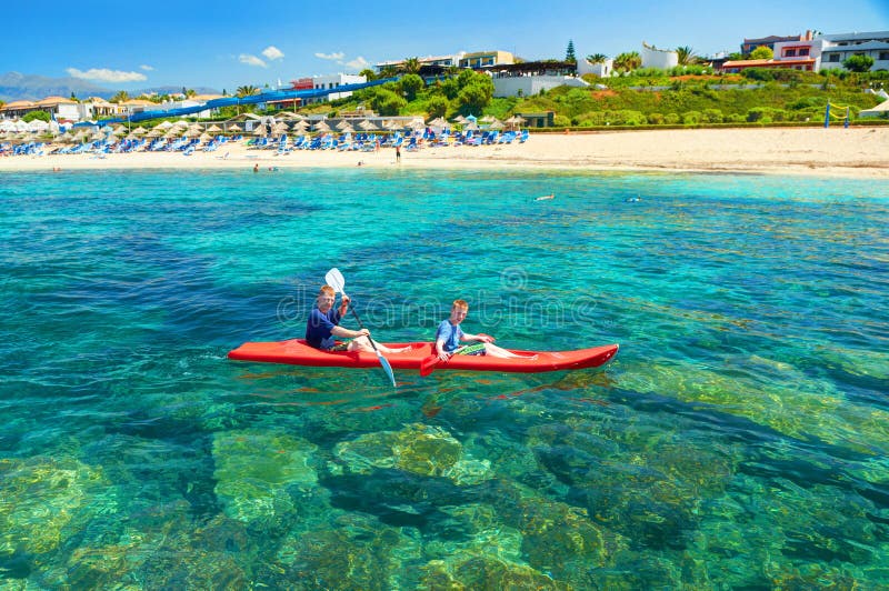 LA GRÈCE, ÎLE DE CRÈTE, JUILLET, 07,2011 : Deux frères de garçons dans le canoë rouge de petit bateau kayak dans l'eau vert-bleu images stock LA GRÈCE, ÎLE DE CRÈTE, JUILLET, 07,2011 : Deux frères de garçons dans le canoë rouge de petit bateau kayak dans l'eau vert-bleu images stock