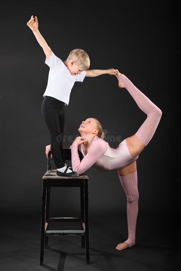 Girl and little boy gymnast took graceful pose at bark chair in black studio. Girl and little boy gymnast took graceful pose at bark chair in black studio