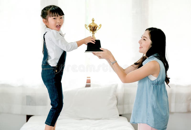 La hija asiática expresa la excitación después de que consiga la recompensa como trofeo de su madre y ella se coloca en la cama b imagen de archivo La hija asiática expresa la excitación después de que consiga la recompensa como trofeo de su madre y ella se coloca en la cama b imagen de archivo