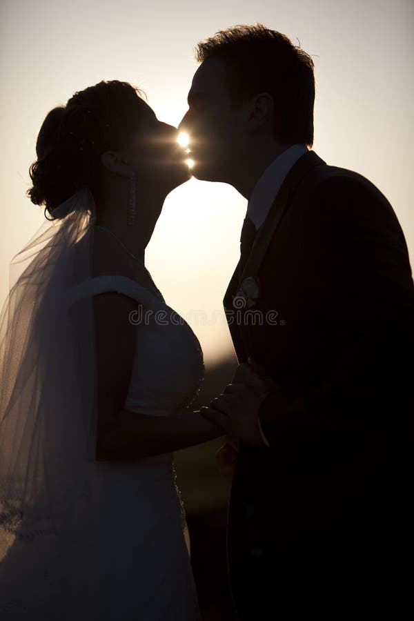 Man holdingkissing woman silhouettes evening park wedding. Man holdingkissing woman silhouettes evening park wedding