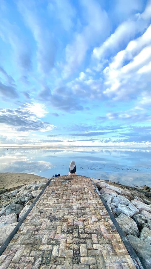 La imagen representa a una persona sentada en un techo como rocas y nubes. la persona parece disfrutar de las vistas al mar. fotografía de archivo libre de regalías