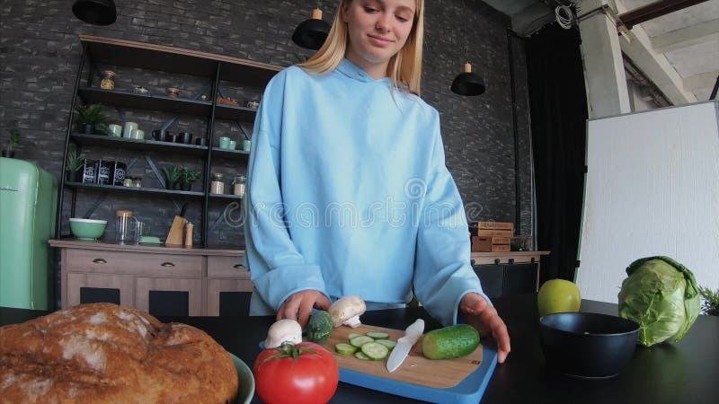 La jeune belle blonde prend des vidéos pendant qu'elle est en train de cuisiner dans la cuisine