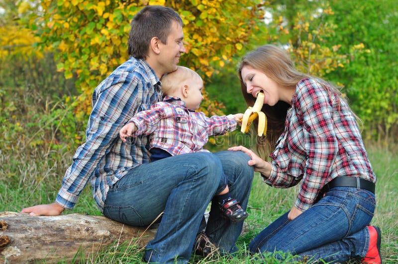 La jeune famille dans le garçon de forêt d'automne traite la banane de maman photographie stock libre de droits La jeune famille dans le garçon de forêt d'automne traite la banane de maman photographie stock libre de droits