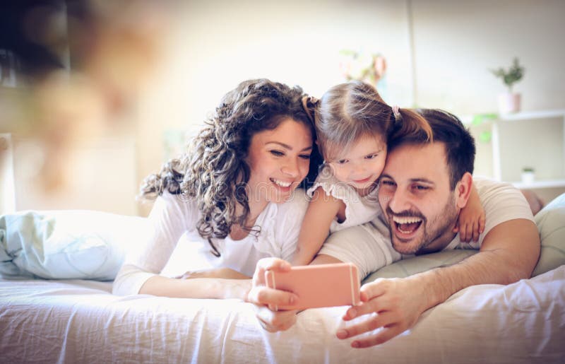 La jeune famille heureuse prennent un autoportrait avec le téléphone intelligent photographie stock La jeune famille heureuse prennent un autoportrait avec le téléphone intelligent photographie stock