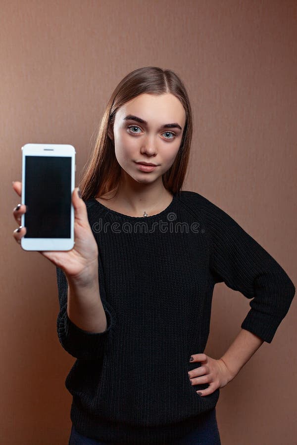 La jeune femme attirante se dirige sur l'écran vide du téléphone dans sa main photographie stock libre de droits La jeune femme attirante se dirige sur l'écran vide du téléphone dans sa main photographie stock libre de droits