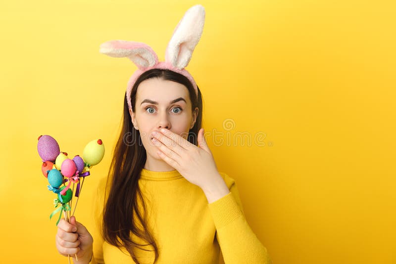 La jeune femme choquée effrayée voit les prises de caméra a peint des oeufs sur les bâtonnets couvre la bouche de main étant lapin images libres de droits