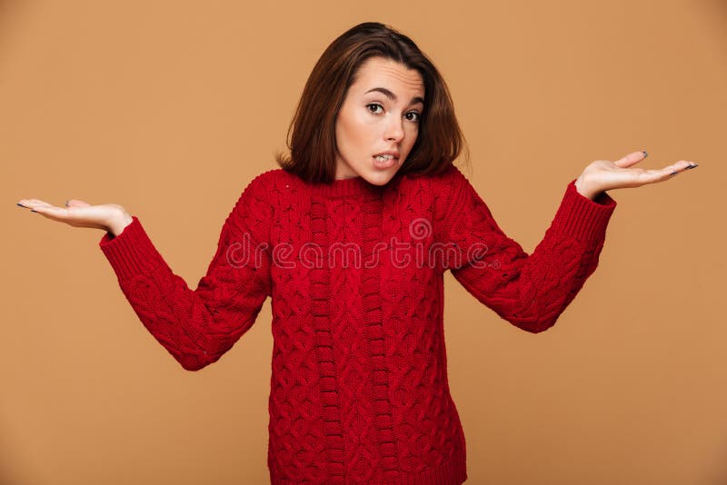 La jeune femme confuse de brune en rouge a tricoté le chandail tenant des WI images libres de droits La jeune femme confuse de brune en rouge a tricoté le chandail tenant des WI images libres de droits