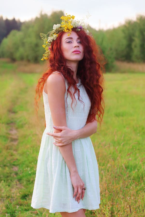 La jeune femme dans la guirlande et la robe de short pose sur le pré à photo libre de droits La jeune femme dans la guirlande et la robe de short pose sur le pré à photo libre de droits