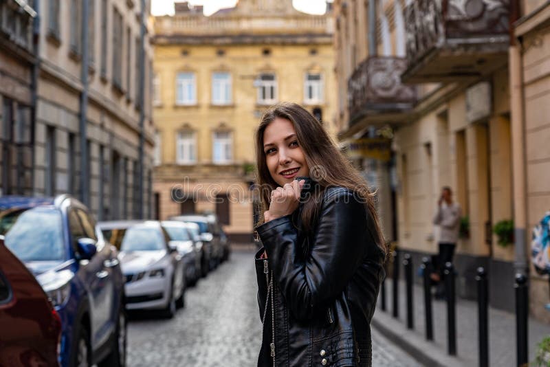 La jeune femme dans la veste en cuir noire est des sourires heureux sur la rue de la ville de Lviv Photographie de portrait photographie stock libre de droits La jeune femme dans la veste en cuir noire est des sourires heureux sur la rue de la ville de Lviv Photographie de portrait photographie stock libre de droits