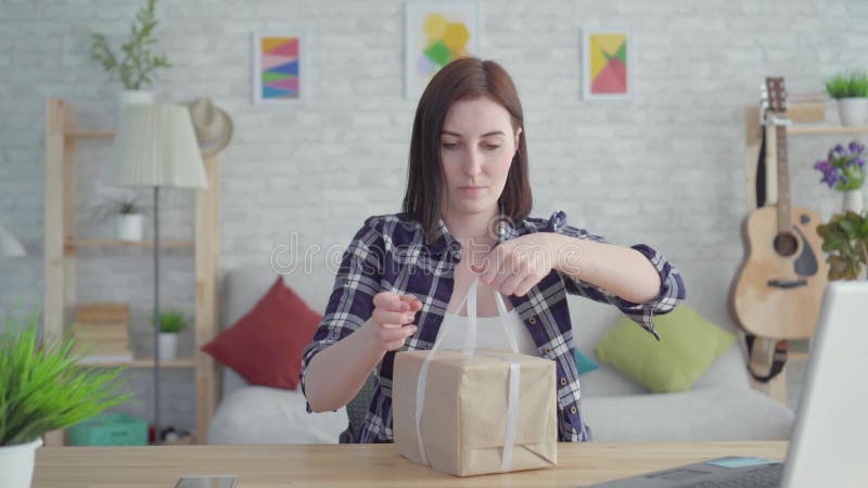 La jeune femme de portrait enveloppe un cadeau se reposant à la table banque de vidéos