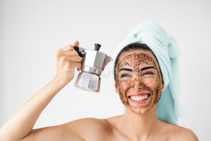 Young smiling woman applying coffee scrub mask on face - Happy girl having healthy skin care spa day at home - Alternative natural exfoliation treatment and people lifestyle concept. Young smiling woman applying coffee scrub mask on face - Happy girl having healthy skin care spa day at home - Alternative natural exfoliation treatment and people lifestyle concept