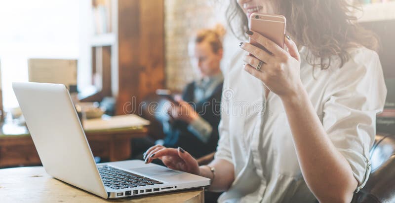 La jeune femme de sourire d'affaires dans une chemise blanche s'assied à la table en café et utilise l'ordinateur portable tout e photos stock