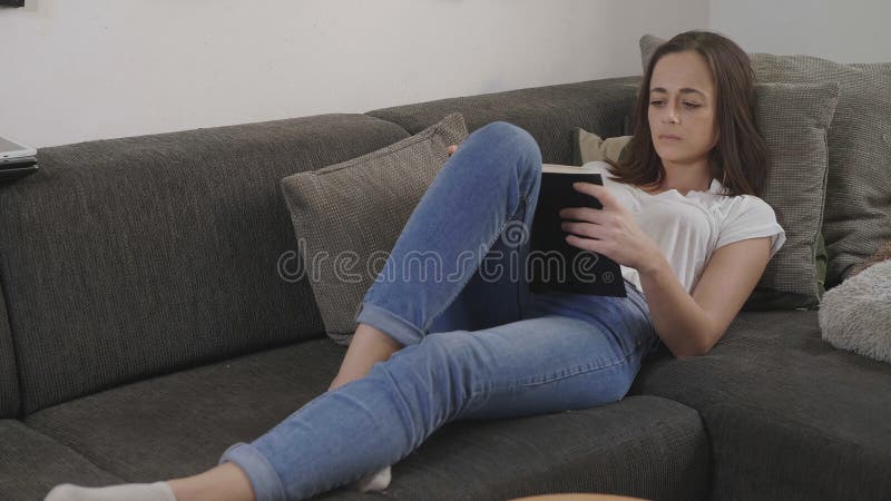 La jeune femme détend dans le salon tout en lisant un livre image stock La jeune femme détend dans le salon tout en lisant un livre image stock