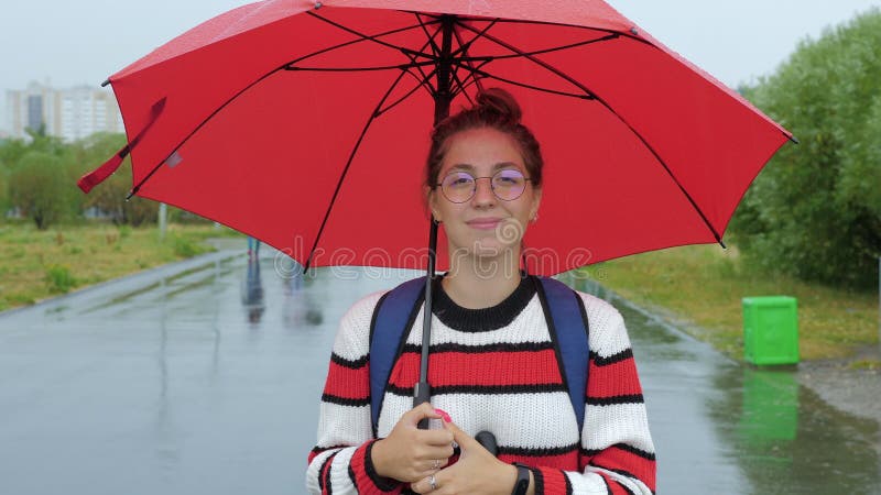 La jeune femme est sous le parapluie rouge au bord de la route banque de vidéos