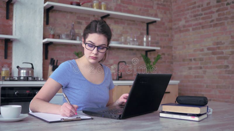 La jeune femme moderne travaillant à la maison, la fille dans des lunettes dactylographiant sur le clavier d'ordinateur portable