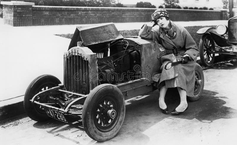 La jeune femme s'asseyant à côté de la petite voiture regardant le moteur sont incroyantes dedans (toutes les personnes représent photo stock La jeune femme s'asseyant à côté de la petite voiture regardant le moteur sont incroyantes dedans (toutes les personnes représent photo stock