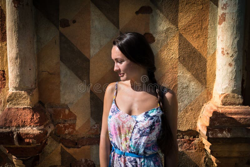 La jeune femme songeuse se tient devant le vieux mur image stock La jeune femme songeuse se tient devant le vieux mur image stock