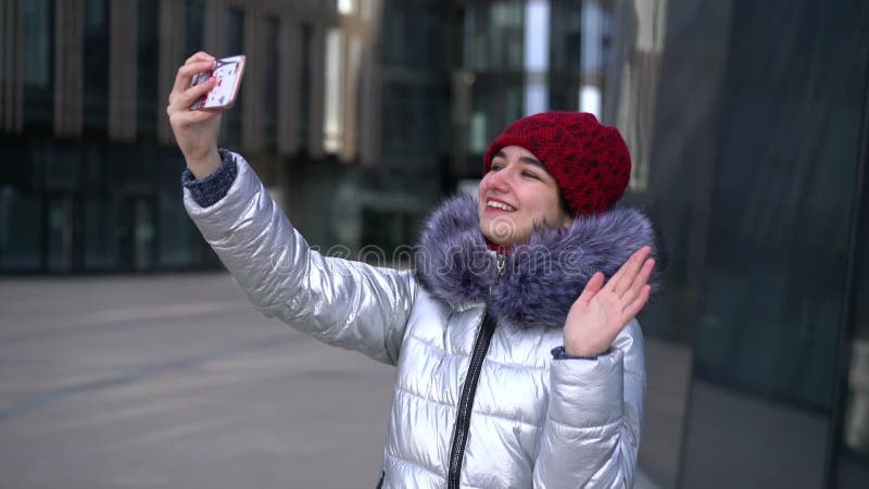 La jeune femme sourit et salue dans la rue communique en communication vidéo clips vidéos