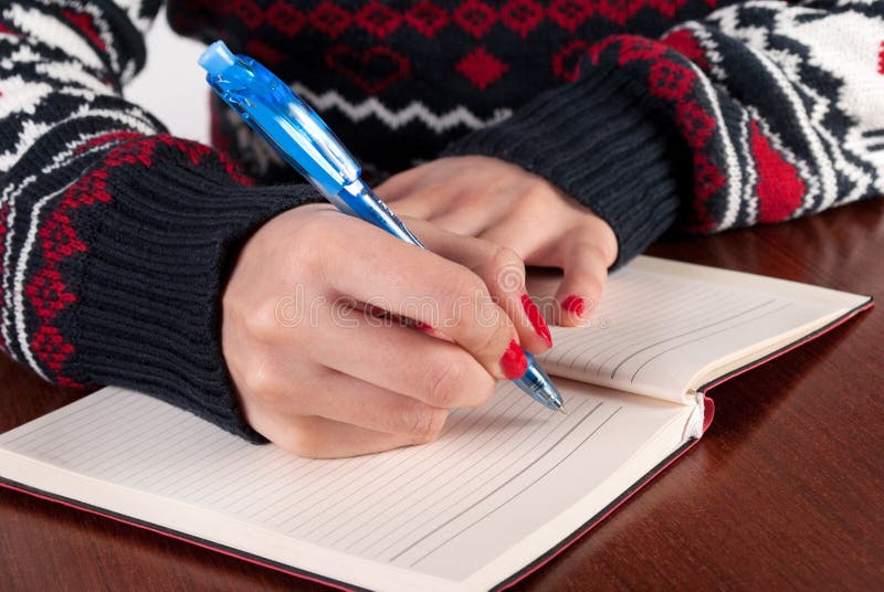 La jeune femme écrit avec le crayon dans le carnet sur le bureau en bois image libre de droits La jeune femme écrit avec le crayon dans le carnet sur le bureau en bois image libre de droits