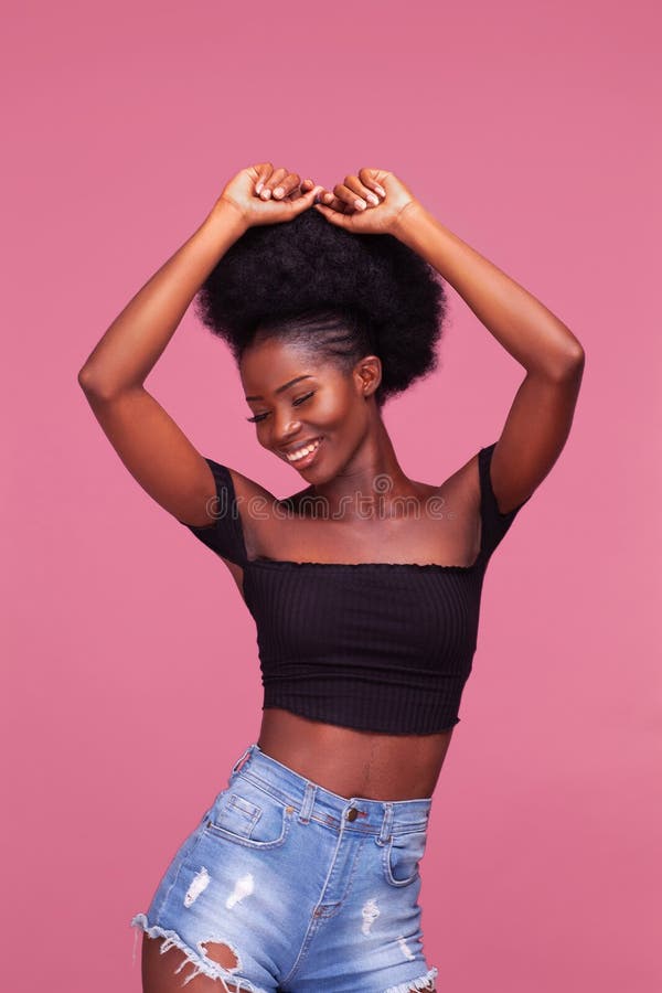 Gorgeous young African American girl with afro hair posing with arms lifted up dressed in black top and denim jeans on dirty pink background. Gorgeous young African American girl with afro hair posing with arms lifted up dressed in black top and denim jeans on dirty pink background.