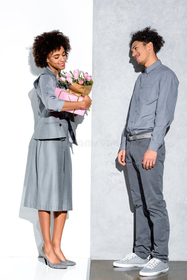 La jeune fille amercian africaine tenant le bouquet des fleurs et du cadeau s'est présentée par l'homme de sourire photo libre de droits La jeune fille amercian africaine tenant le bouquet des fleurs et du cadeau s'est présentée par l'homme de sourire photo libre de droits
