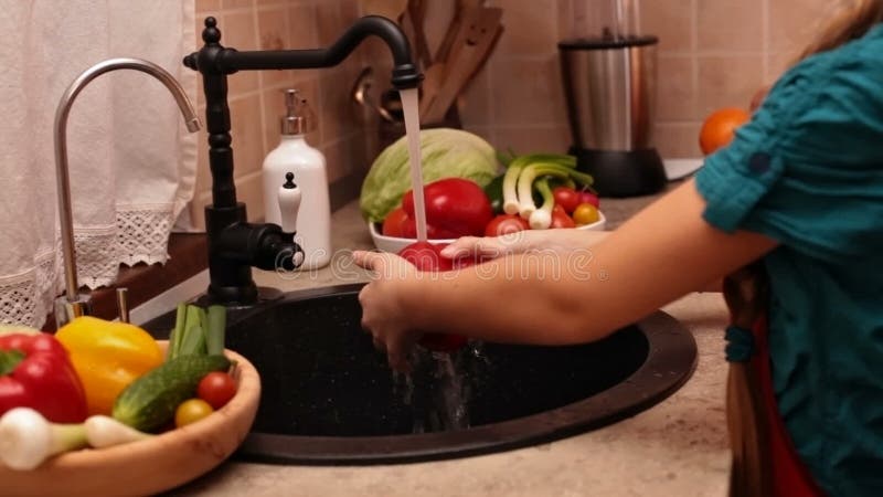 La jeune fille remet les légumes de lavage à l'évier de cuisine banque de vidéos