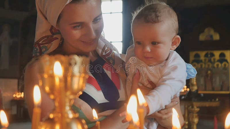 La jeune mère avec le bébé observe les bougies brûlantes dans l'église dans au ralenti