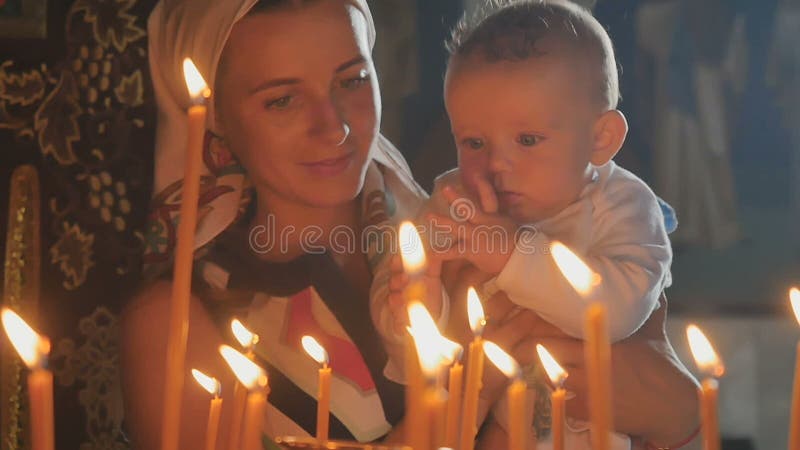 La jeune mère avec le petit fils observe des bougies d'un burning dans l'église