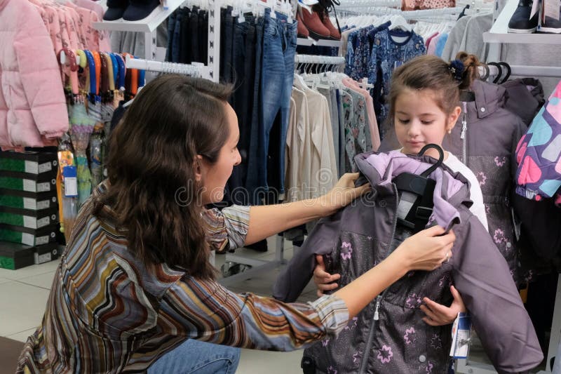 La jeune mère essaye les vêtements des enfants pour l'automne Préparation à la saison d'hiver avec un enfant Achetez une veste ch photo libre de droits La jeune mère essaye les vêtements des enfants pour l'automne Préparation à la saison d'hiver avec un enfant Achetez une veste ch photo libre de droits