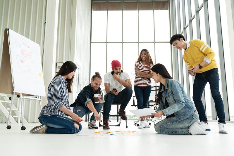 La jeune réunion de groupe diverse créative et regarder le plan de projet présentent sur le plancher discutent ou font un brainst photos stock