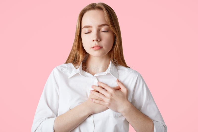 La jolie adolescente garde des mains sur le coffre et les yeux fermés, étant reconnaissants et reconnaissants, exprime sa dévotio photos stock La jolie adolescente garde des mains sur le coffre et les yeux fermés, étant reconnaissants et reconnaissants, exprime sa dévotio photos stock