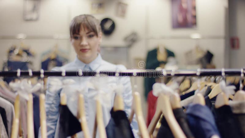 La jolie femme adulte marche au support des vêtements dans un magasin pour rechercher la nouvelle robe