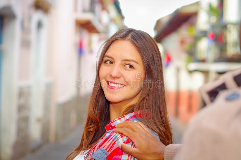 La jolie femme de brune tourne autour le sourire tandis que la main de boyrfriends touche son épaule, couleurs vibrantes et urbai photographie stock libre de droits La jolie femme de brune tourne autour le sourire tandis que la main de boyrfriends touche son épaule, couleurs vibrantes et urbai photographie stock libre de droits