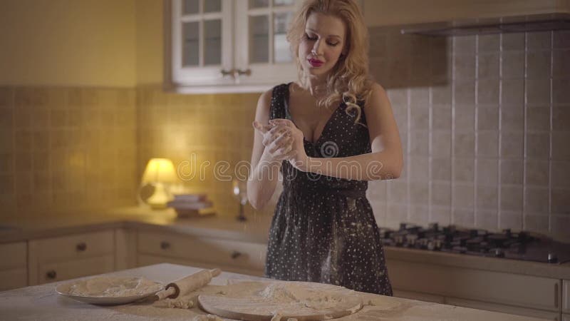 La jolie femme séduisante dans la robe noire enduite de la pâte de mélange de farine dans des mains et jette avec force la pâte d banque de vidéos
